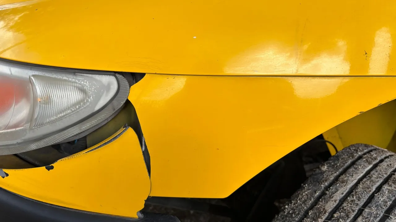 Atelier de carrosserie avec voiture sur pont élévateur et carrossier en pleine réparation